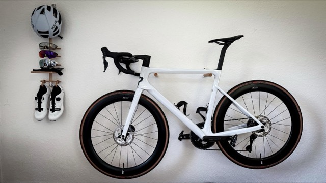 Road bike on a wooden wall mount, with helmet, glasses and shoes hung alongside